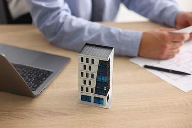 Photo of Real estate agent with paperwork, apartment building model and laptop at wooden table, closeup