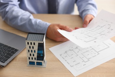 Photo of Real estate agent with architectural drawings, apartment building model and laptop at wooden table, closeup