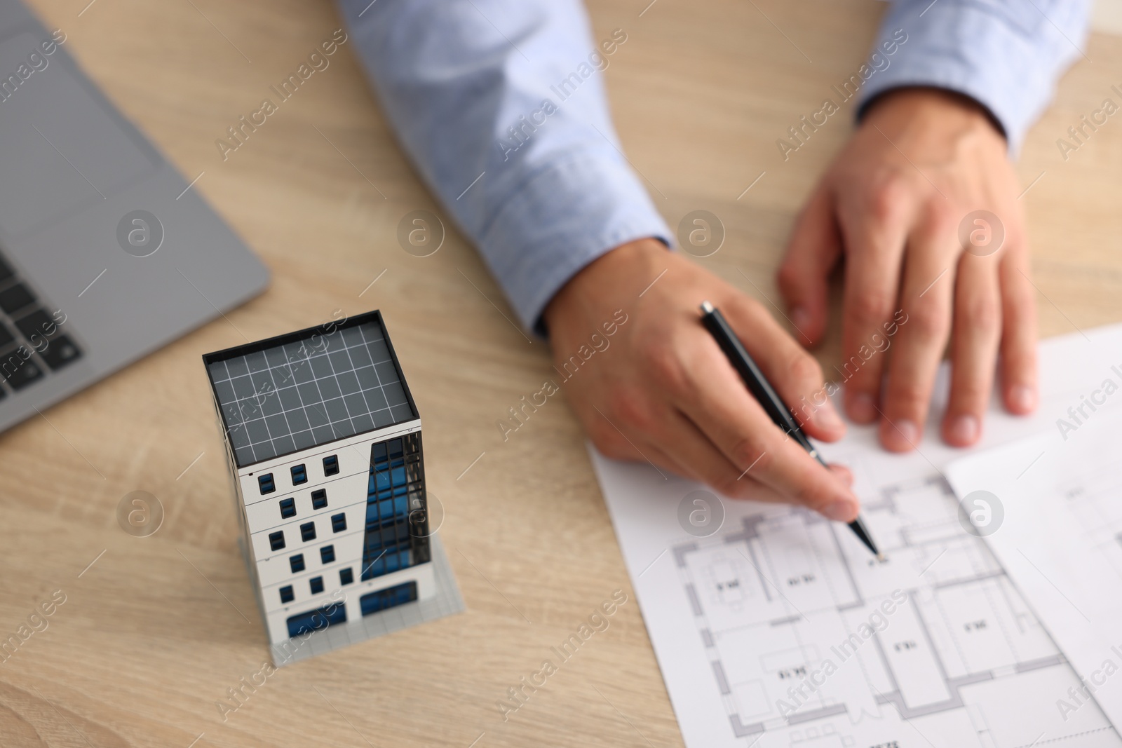 Photo of Real estate agent with architectural drawings, apartment building model and laptop at wooden table, above view