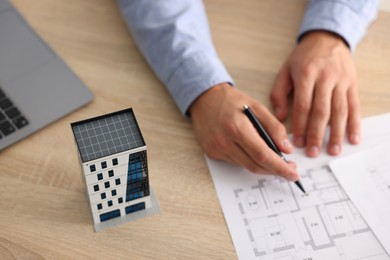 Photo of Real estate agent with architectural drawings, apartment building model and laptop at wooden table, above view