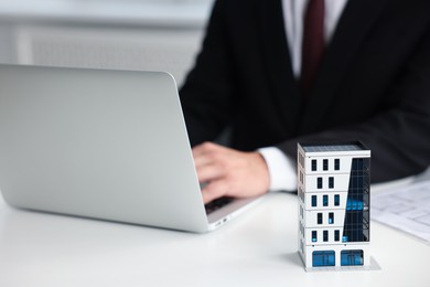 Photo of Real estate agent working with laptop at white table, focus on apartment building model