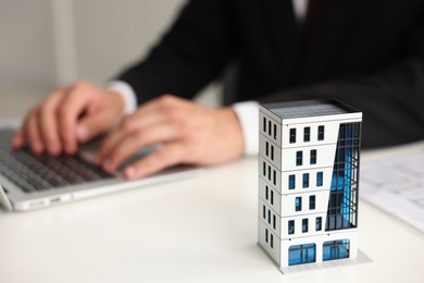 Photo of Real estate agent working with laptop at white table, focus on apartment building model