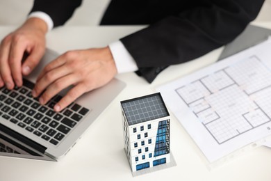 Photo of Real estate agent with architectural drawing, apartment building model and laptop at white table, above view
