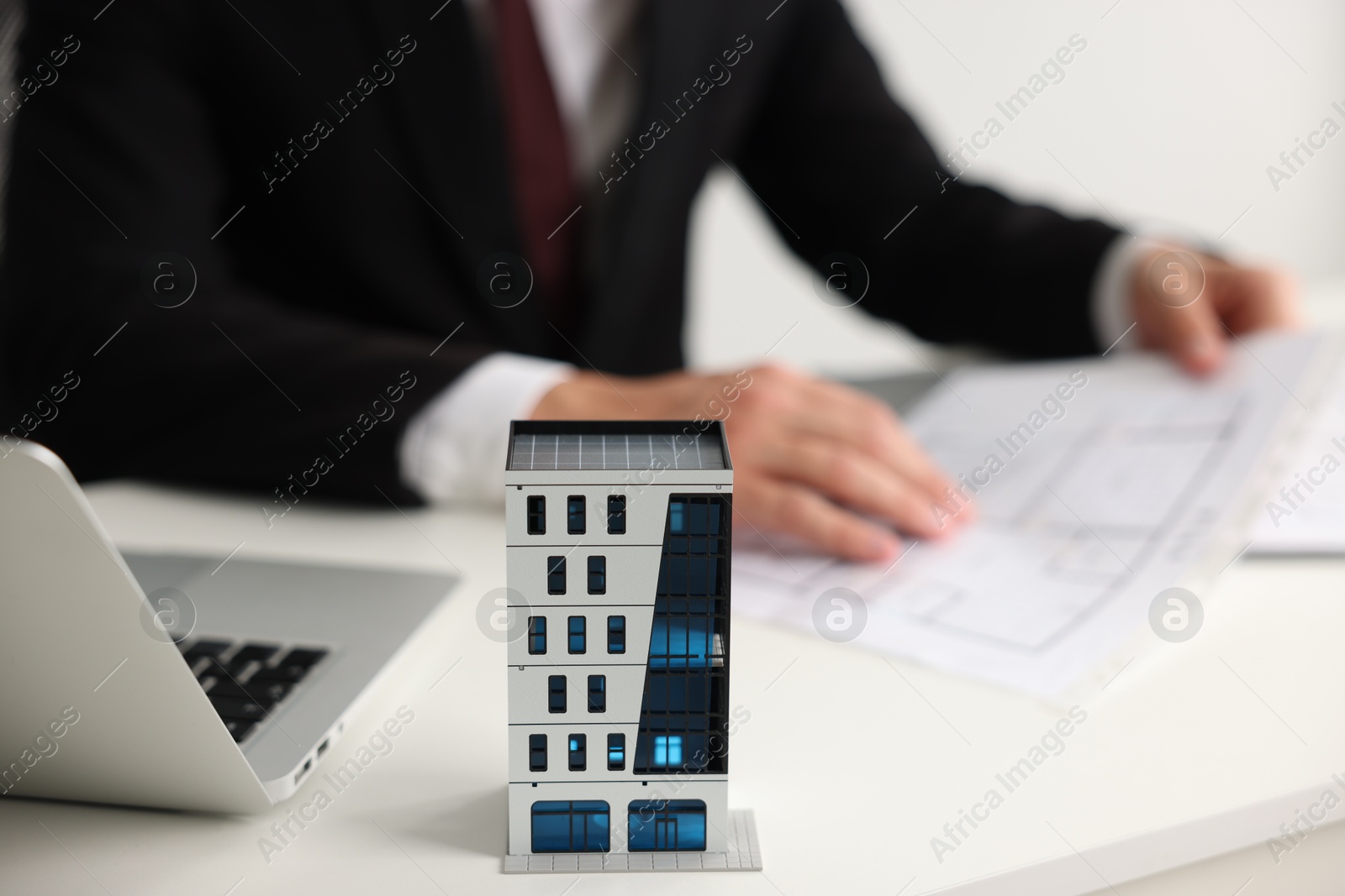 Photo of Real estate agent with architectural drawing, apartment building model and laptop at white table, closeup