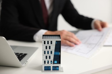 Photo of Real estate agent with architectural drawing, apartment building model and laptop at white table, closeup