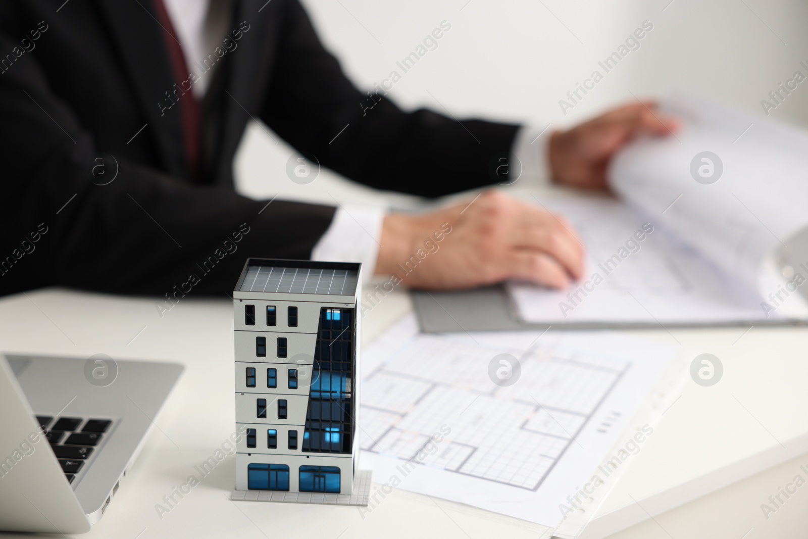 Photo of Real estate agent with architectural drawings, apartment building model and laptop at white table, closeup