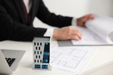Photo of Real estate agent with architectural drawings, apartment building model and laptop at white table, closeup