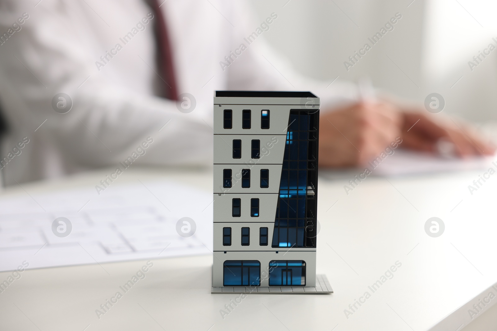Photo of Real estate agent with paperwork at white table, focus on apartment building model