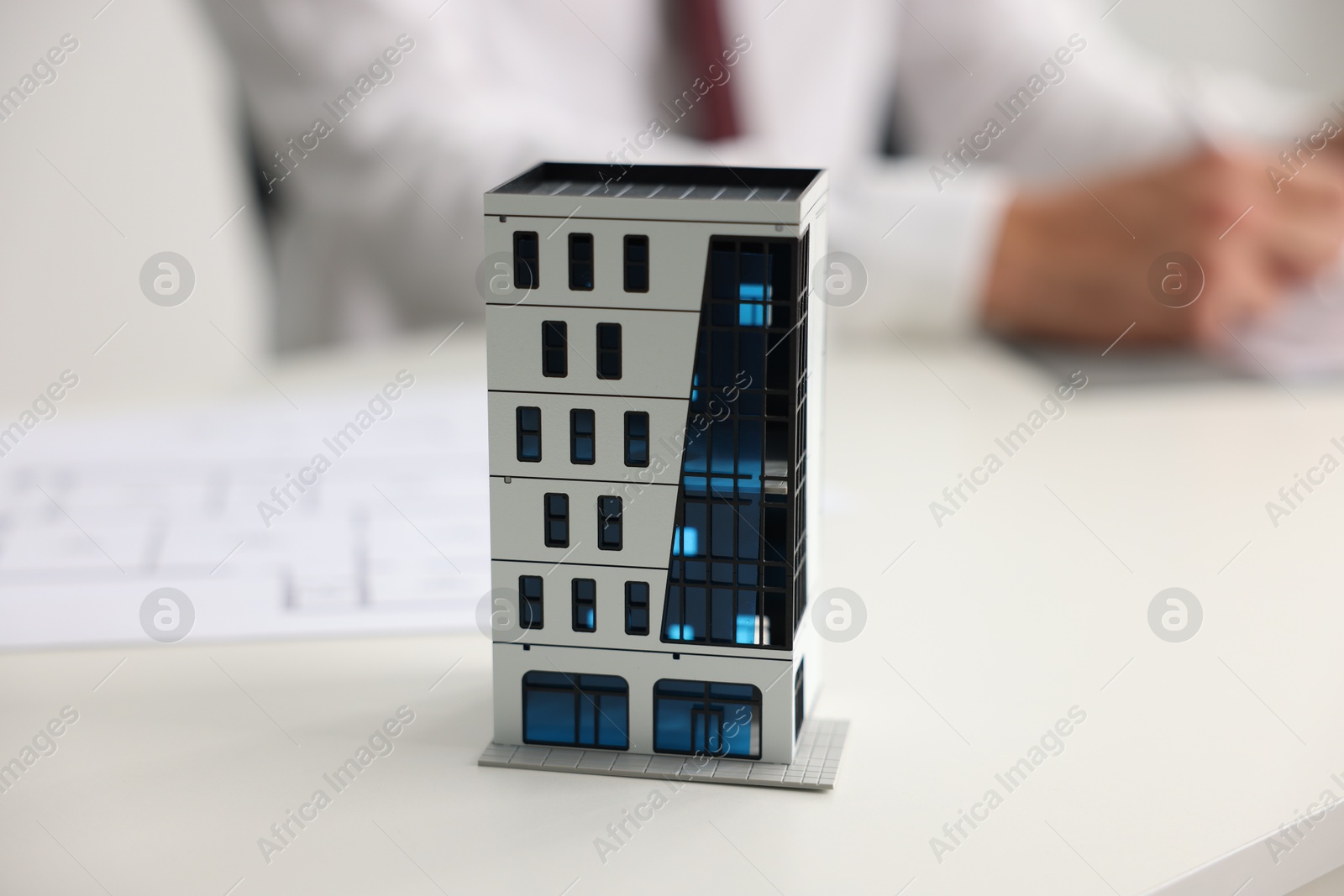 Photo of Real estate agent with paperwork at white table, focus on apartment building model