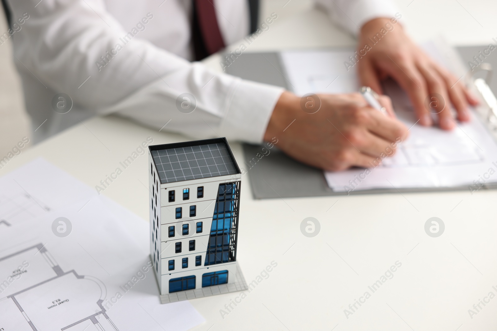 Photo of Real estate agent with paperwork at white table, focus on apartment building model