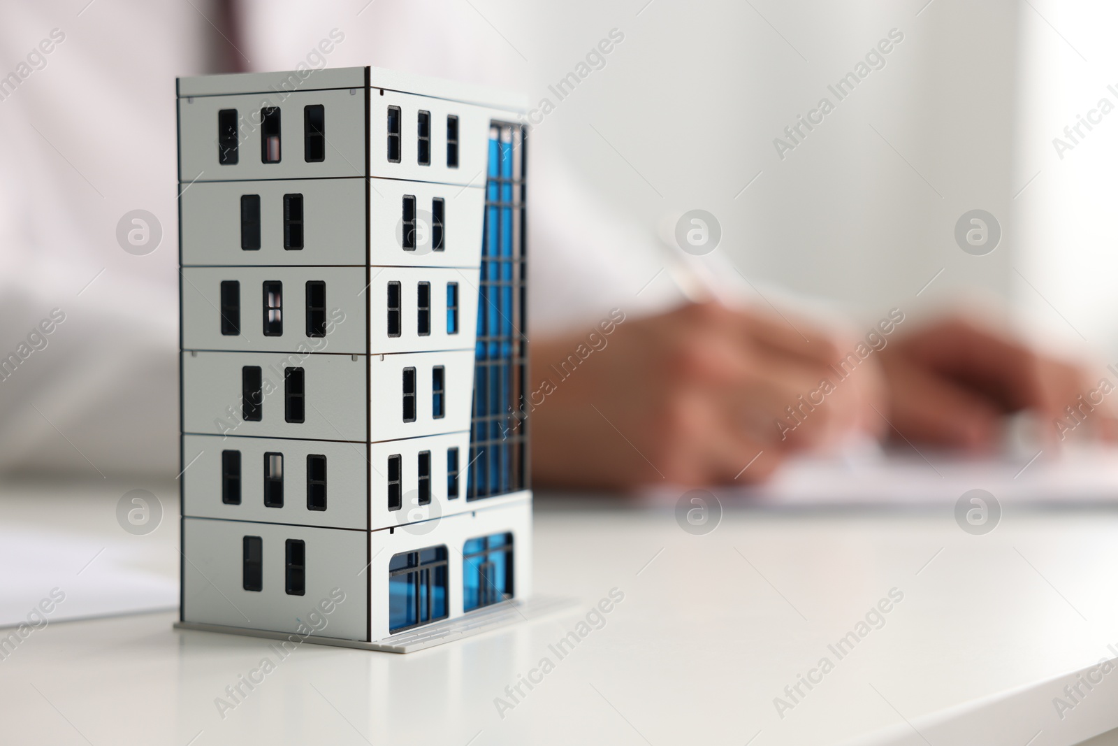 Photo of Real estate agent with paperwork at white table, focus on apartment building model