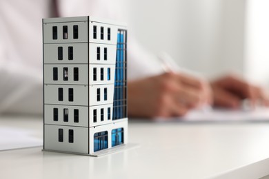 Photo of Real estate agent with paperwork at white table, focus on apartment building model