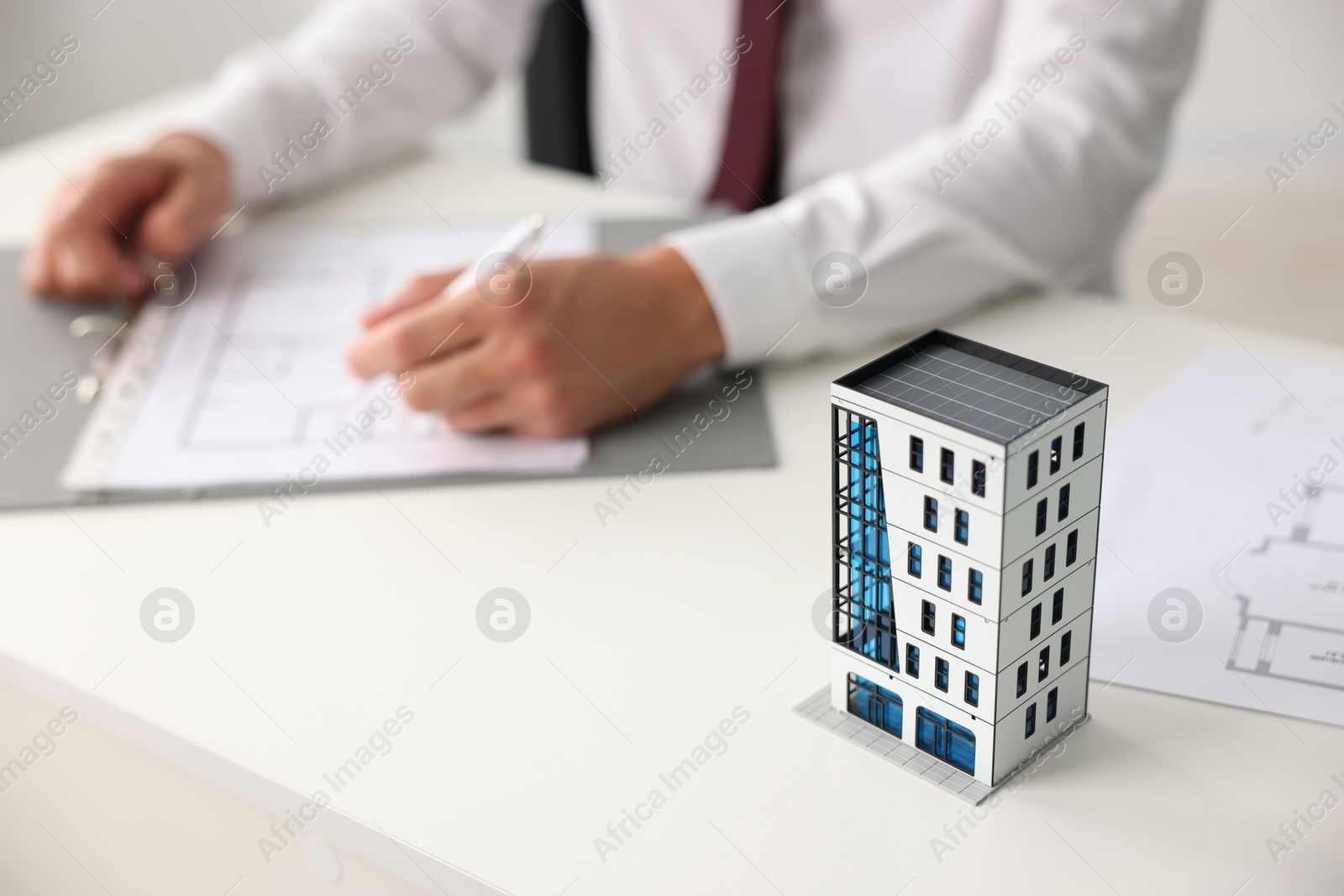 Photo of Real estate agent with paperwork at white table, focus on apartment building model