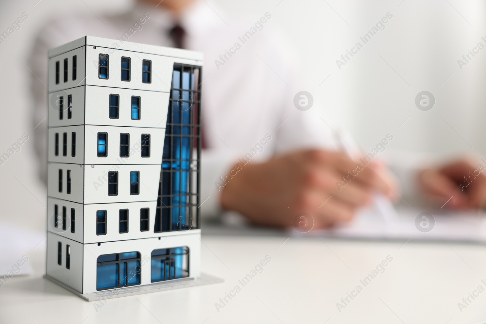 Photo of Real estate agent with paperwork at white table, focus on apartment building model