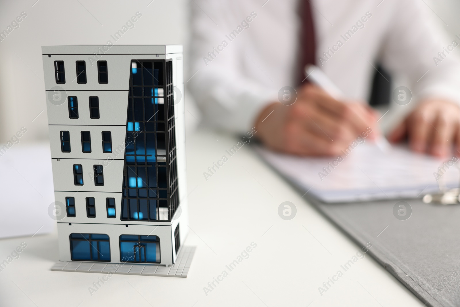 Photo of Real estate agent with paperwork at white table, focus on apartment building model