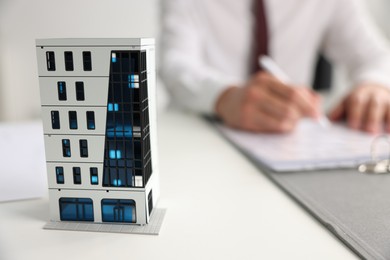 Photo of Real estate agent with paperwork at white table, focus on apartment building model