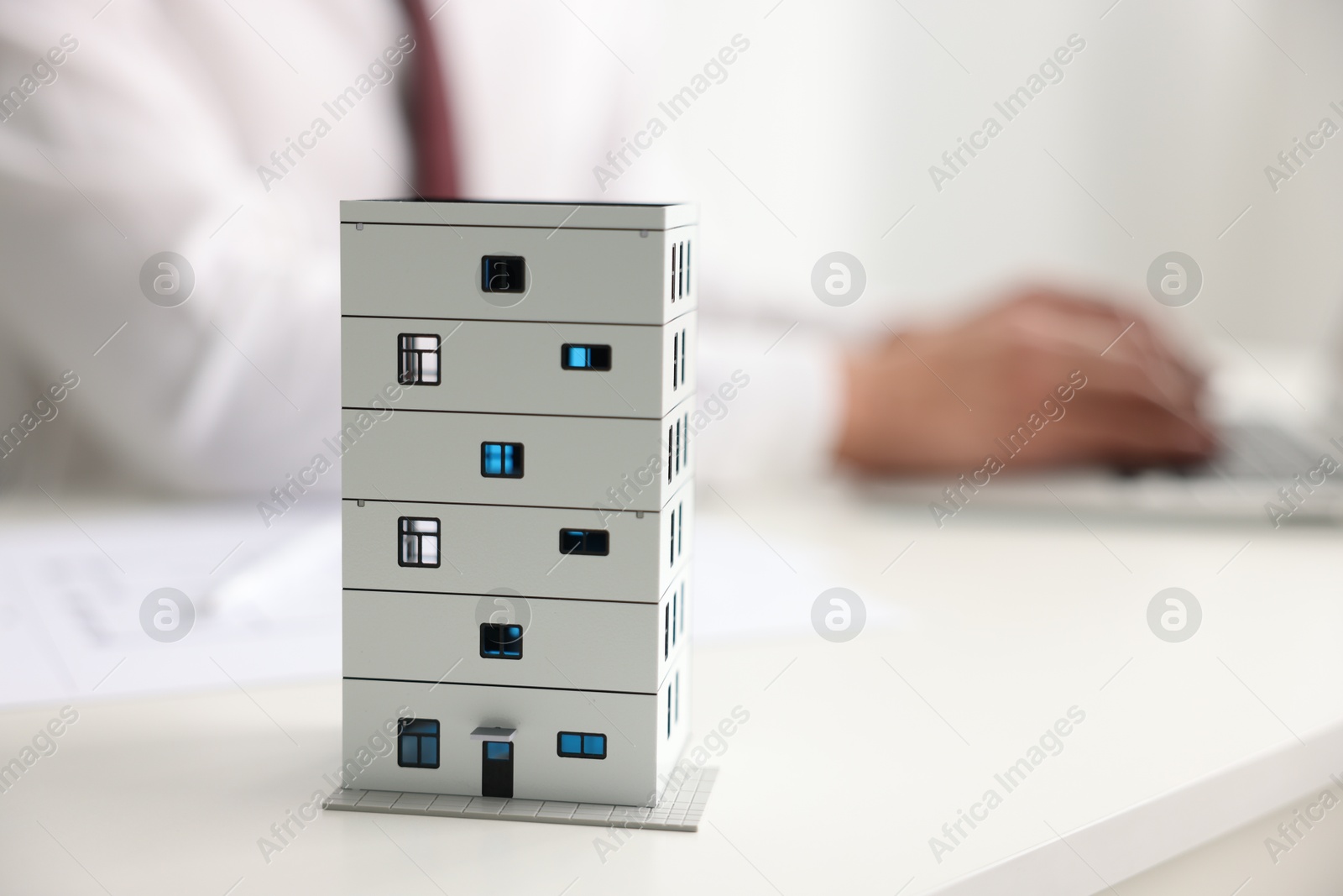 Photo of Real estate agent working laptop at white table, focus on apartment building model