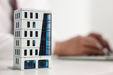 Photo of Real estate agent working laptop at white table, focus on apartment building model