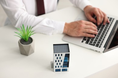 Photo of Real estate agent working with laptop at white table, focus on apartment building model and decorative plant