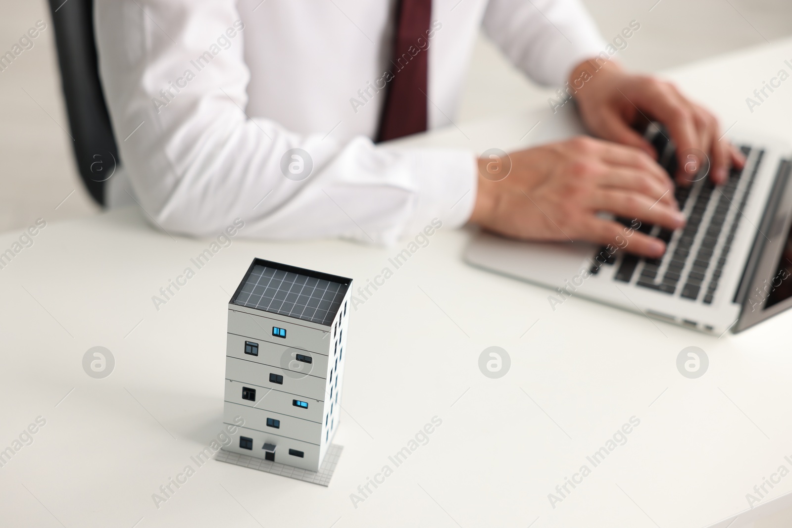 Photo of Real estate agent working with laptop at white table, focus on apartment building model