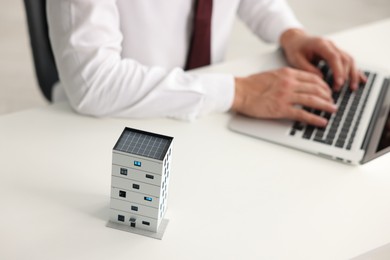 Photo of Real estate agent working with laptop at white table, focus on apartment building model