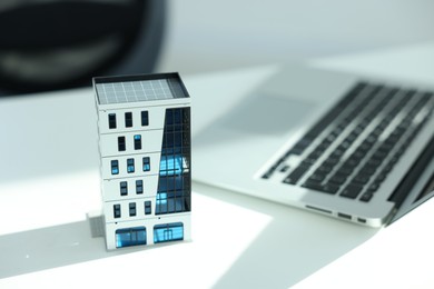 Photo of Real estate. Apartment building model and laptop on white table, closeup