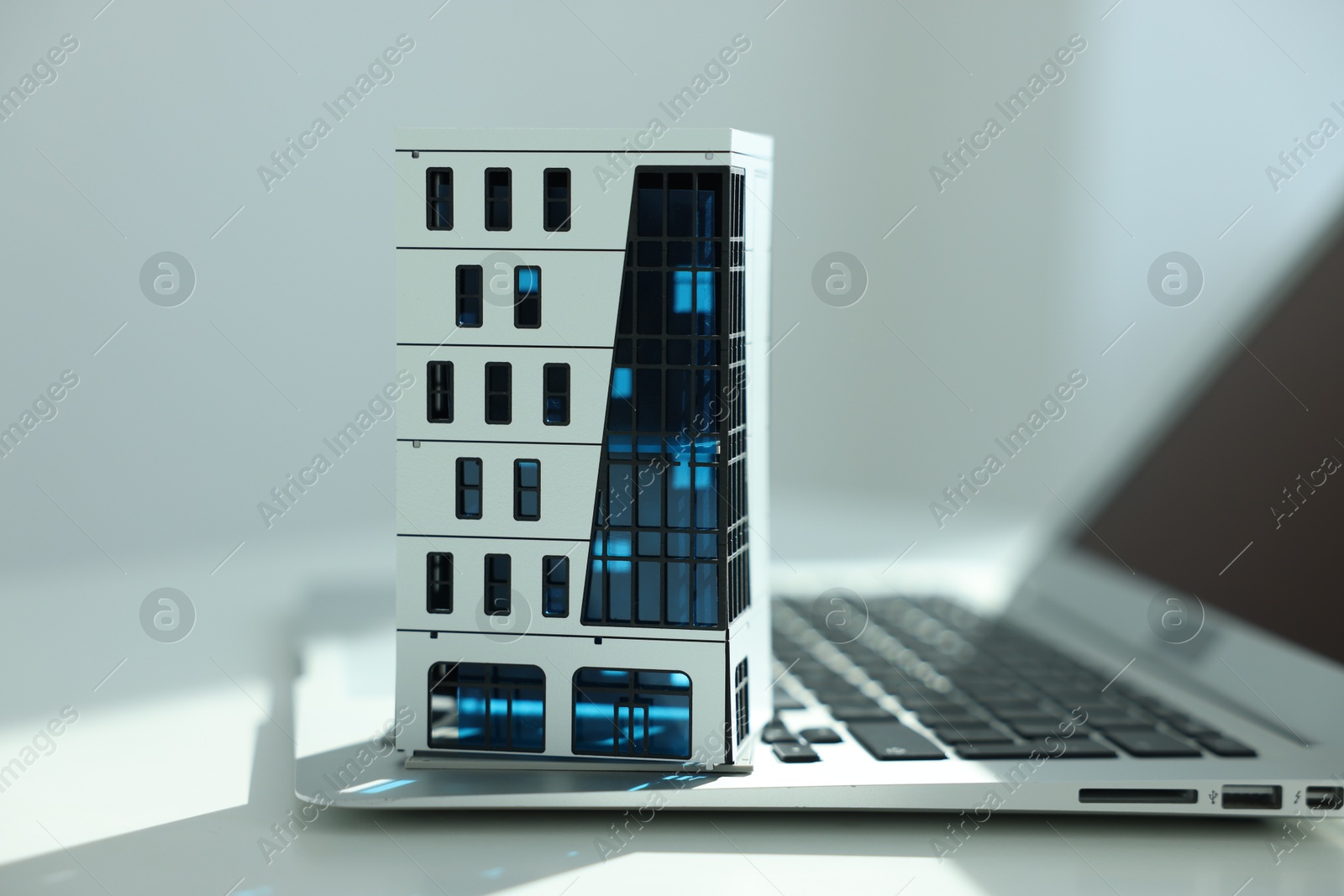 Photo of Real estate. Apartment building model and laptop on light table indoors, closeup