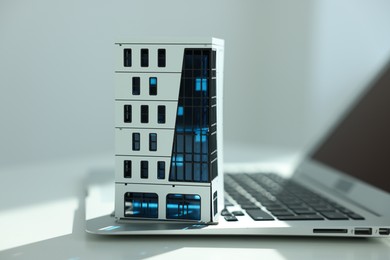 Photo of Real estate. Apartment building model and laptop on light table indoors, closeup