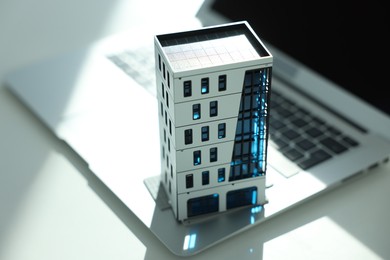 Photo of Real estate. Apartment building model and laptop on light table, closeup