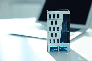 Photo of Real estate. Apartment building model and laptop on light table, closeup