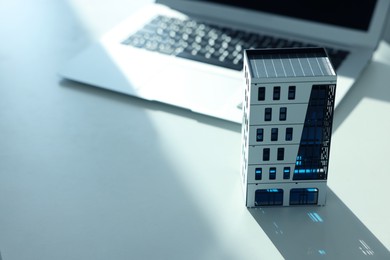 Photo of Real estate. Apartment building model and laptop on light table, closeup