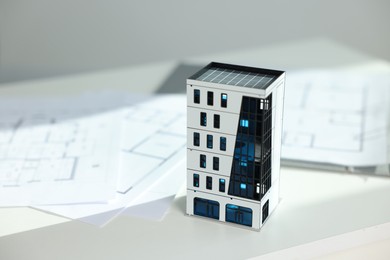 Photo of Real estate. Apartment building model and architectural drawings on white table, closeup