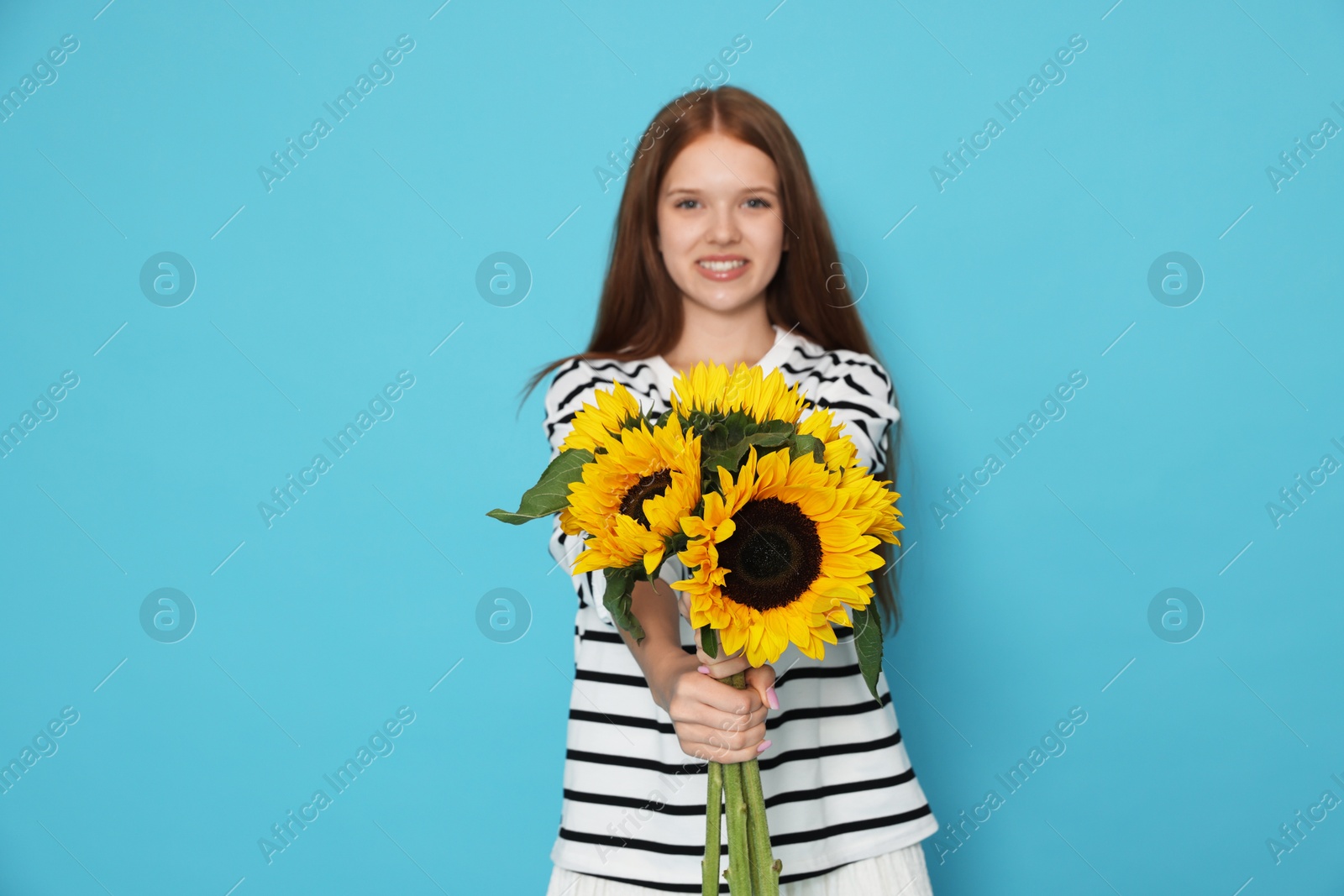 Photo of Teenage girl with bouquet of beautiful sunflowers on light blue background