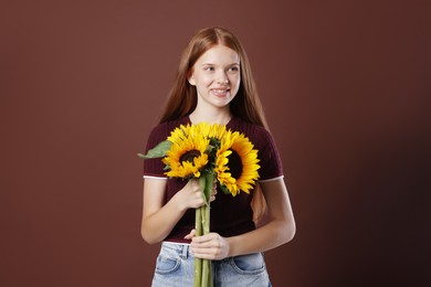 Photo of Teenage girl with bouquet of beautiful sunflowers on brown background
