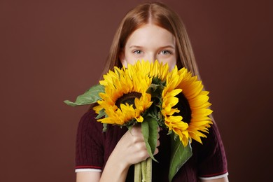 Photo of Teenage girl with bouquet of beautiful sunflowers on brown background