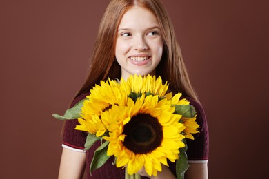 Photo of Teenage girl with bouquet of beautiful sunflowers on brown background
