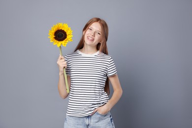 Photo of Teenage girl with beautiful sunflower on grey background