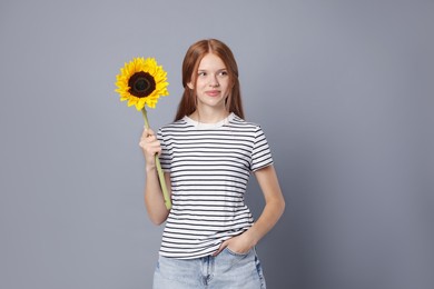 Photo of Teenage girl with beautiful sunflower on grey background