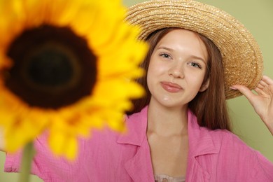 Photo of Teenage girl with beautiful sunflower on green background, selective focus