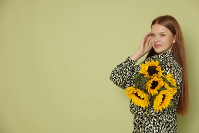 Photo of Teenage girl with bouquet of beautiful sunflowers on green background, space for text