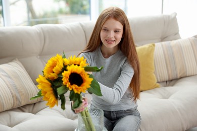 Photo of Teenage girl putting beautiful sunflowers into vase at home