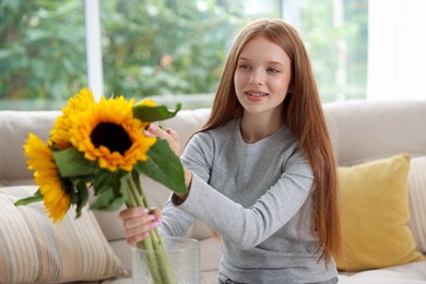 Photo of Teenage girl putting beautiful sunflowers into vase at home