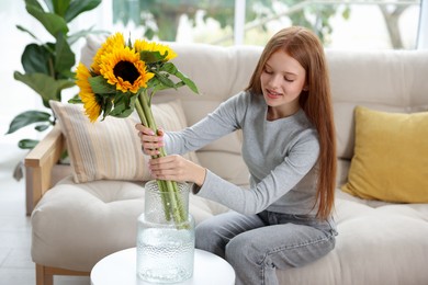 Photo of Teenage girl putting beautiful sunflowers into vase at home