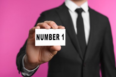 Image of Winner. Man showing card with word Number 1 against pink background, closeup