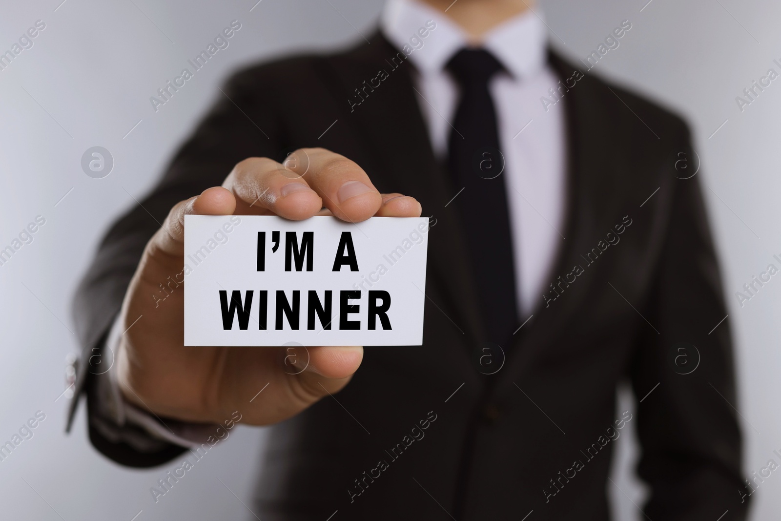 Image of Man showing card with phrase I'm A Winner against white background, closeup