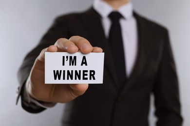 Image of Man showing card with phrase I'm A Winner against white background, closeup
