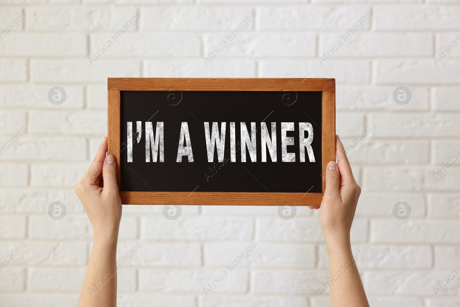 Image of Woman holding chalkboard with phrase I'm A Winner against white brick wall, closeup