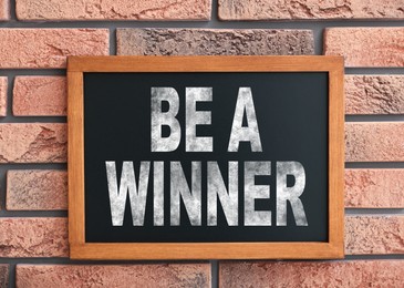 Image of Chalkboard with phrase Be A Winner hanging on brick wall