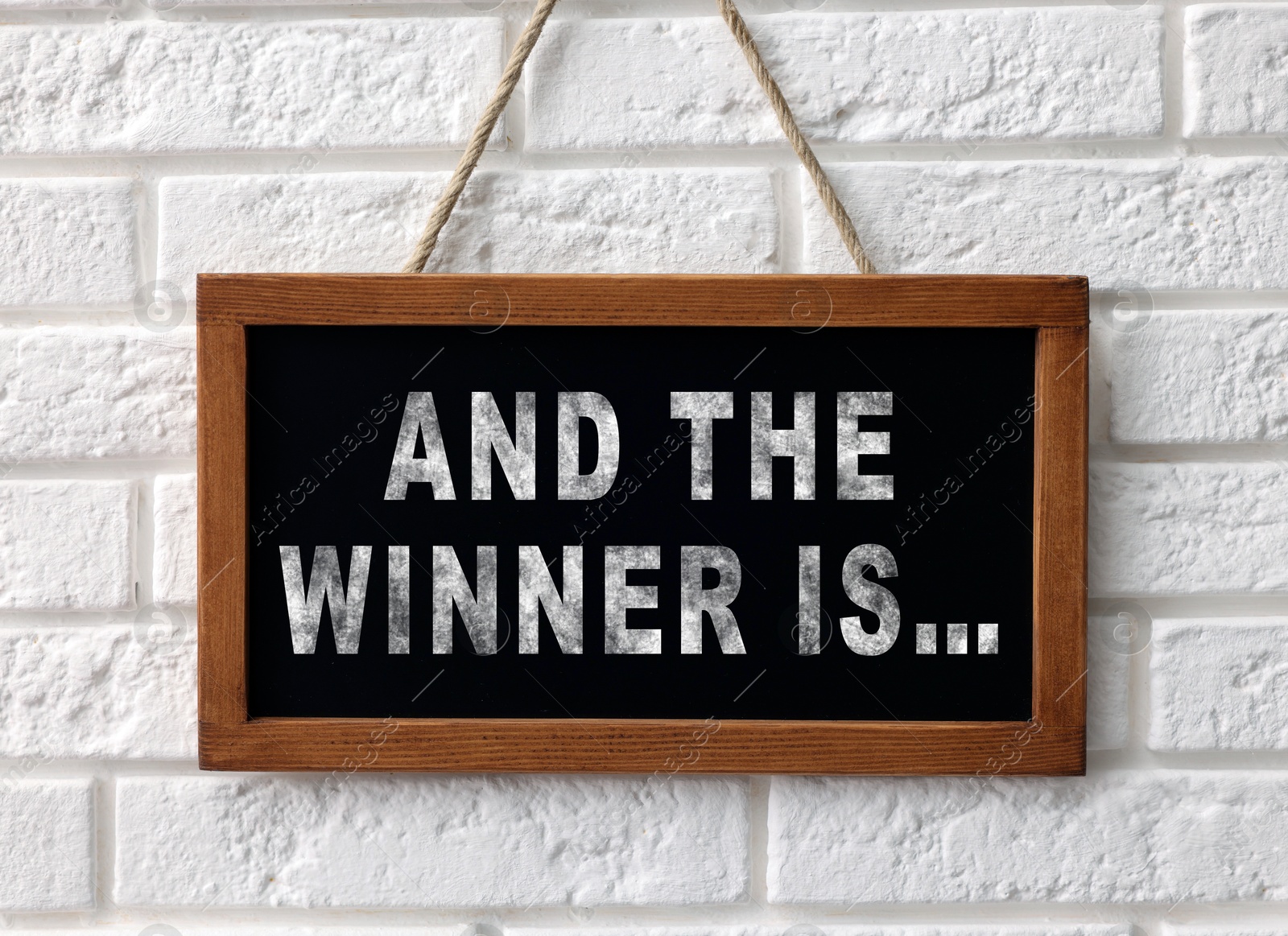 Image of Chalkboard with phrase And The Winner Is hanging on white brick wall