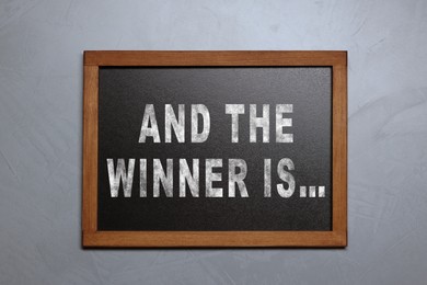 Image of Chalkboard with phrase And The Winner Is hanging on grey wall